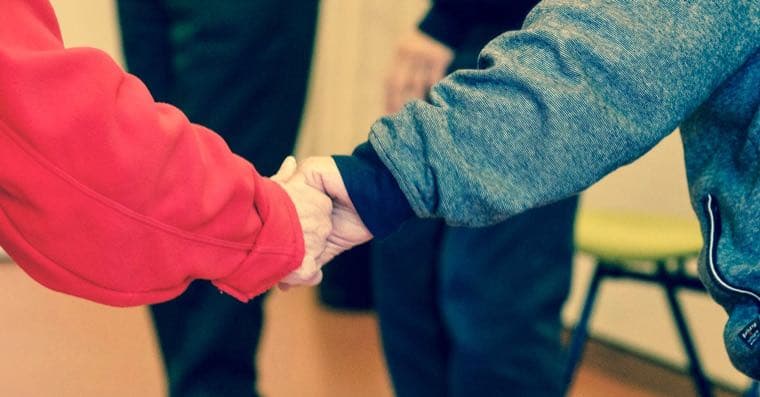 A carer's hands gently resting over the hands of an older person