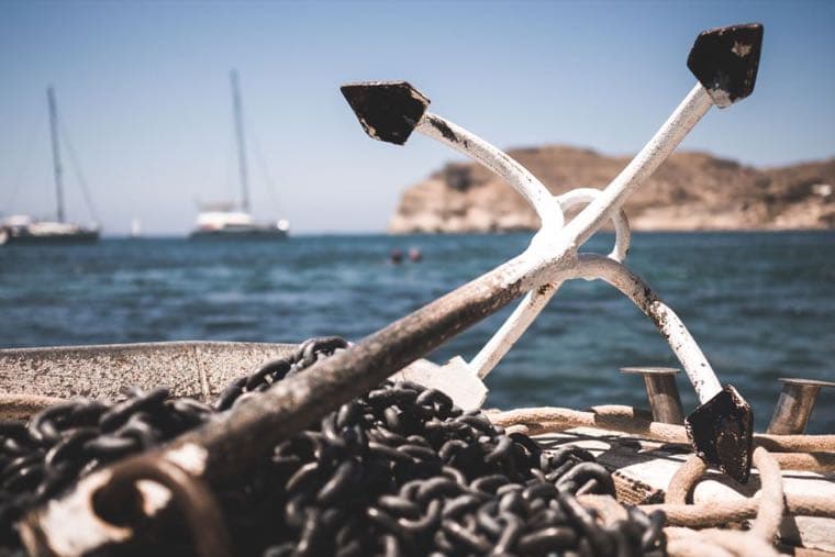 A ship's anchor and its heavy chain on a boat deck, with the sea behind