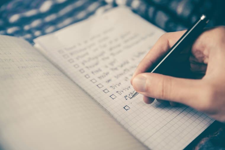 A hand ticking off boxes on a handwritten checklist in a grid notebook