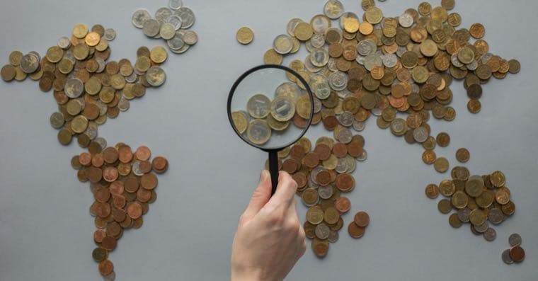 A magnifying glass held over a world map made of coins