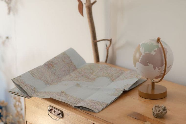 A folded paper world map and a small globe on a wooden desk