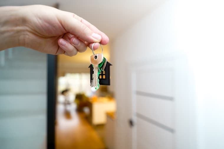 A hand holding house keys with a house-shaped keyring in a home doorway