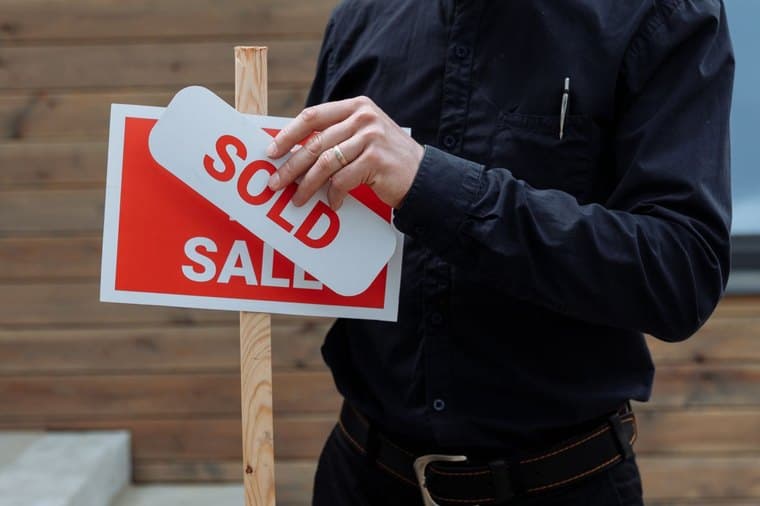A real estate agent placing a sold sticker on a for-sale sign