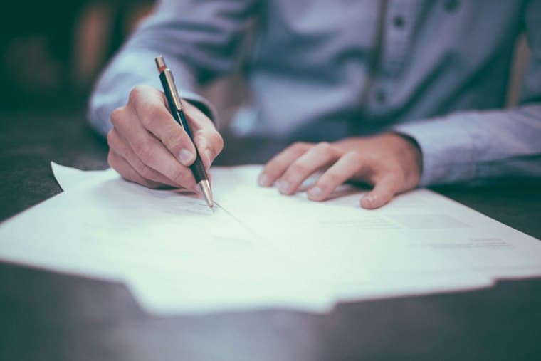A person signing a document at a desk, hands and pen in close focus