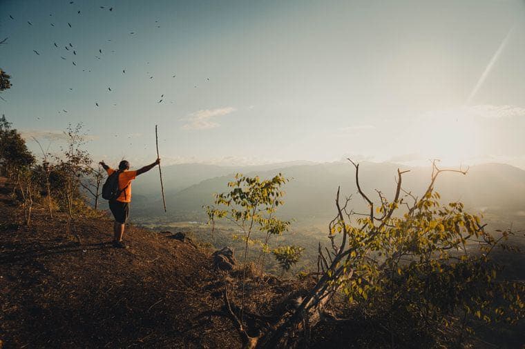 A hiker on a mountain ridge at sunrise with arms raised