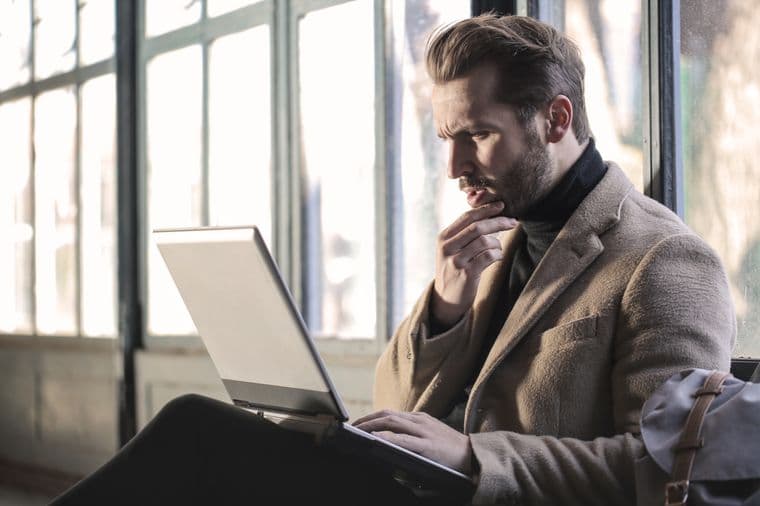 A person thinking carefully while working at a laptop in a bright room