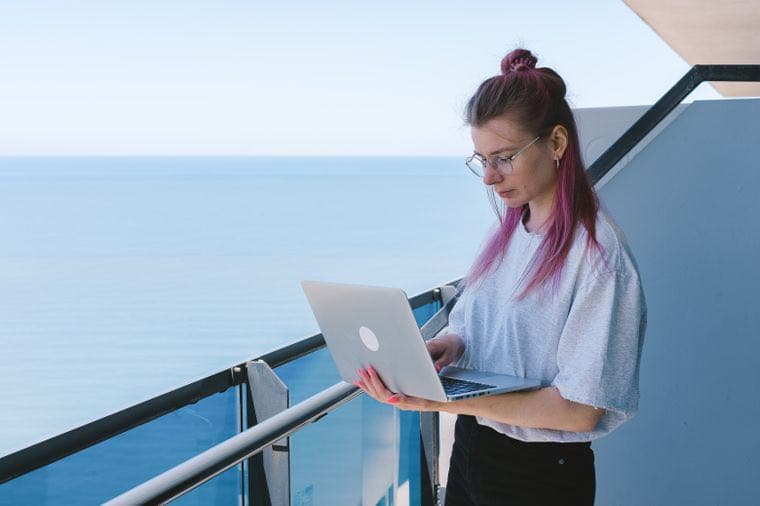 A person working on a laptop on a balcony over the ocean