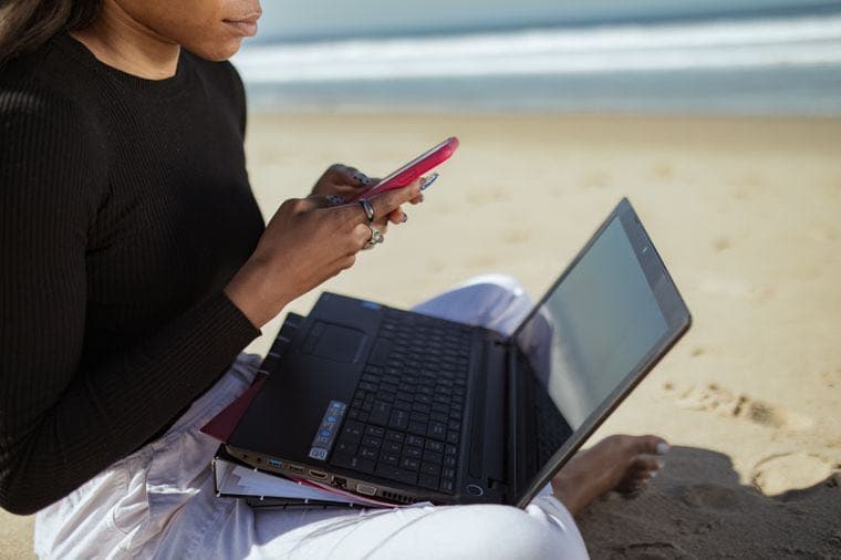 A person working on a laptop and phone on the beach