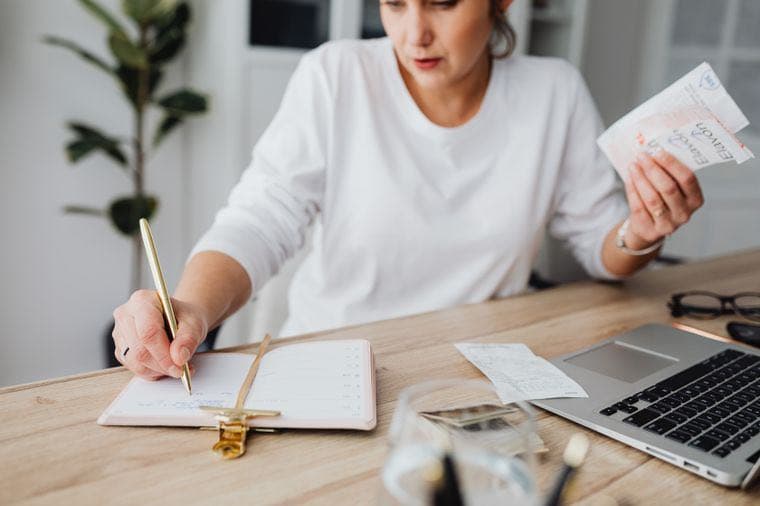A woman writing in a budget planner at her desk with a laptop