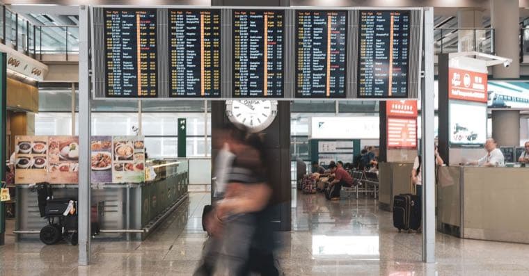 A traveller with a suitcase looking at a departures board at an airport