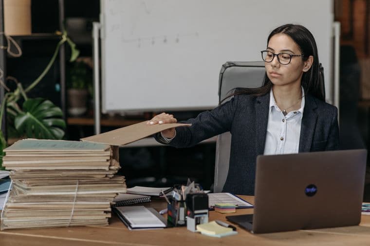 Someone adding a folder to a stack of files on a desk