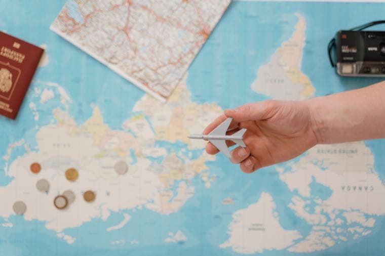 A hand holding a toy plane over a world map with a passport and coins