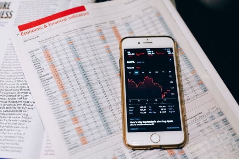 A phone showing a share trading app resting on a financial newspaper