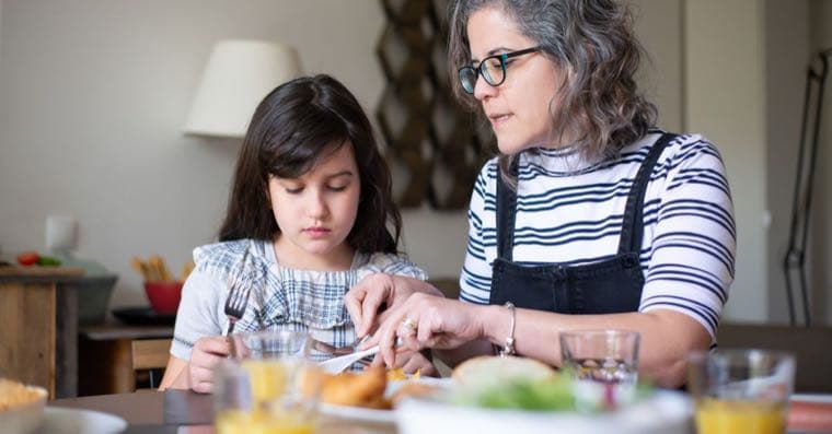 An adult child and an elderly parent talking over tea at a kitchen table
