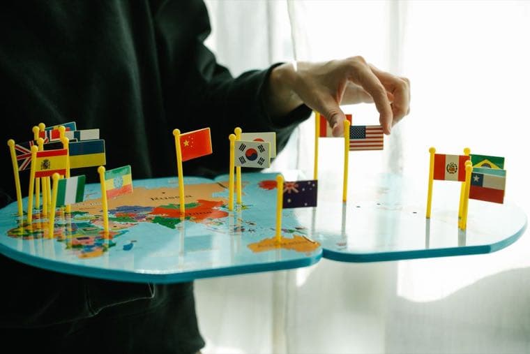 A hand placing the United States flag among many other country flags on a world map