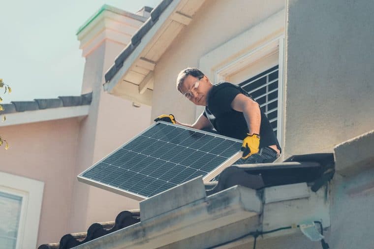 A person installing a solar panel on a house roof