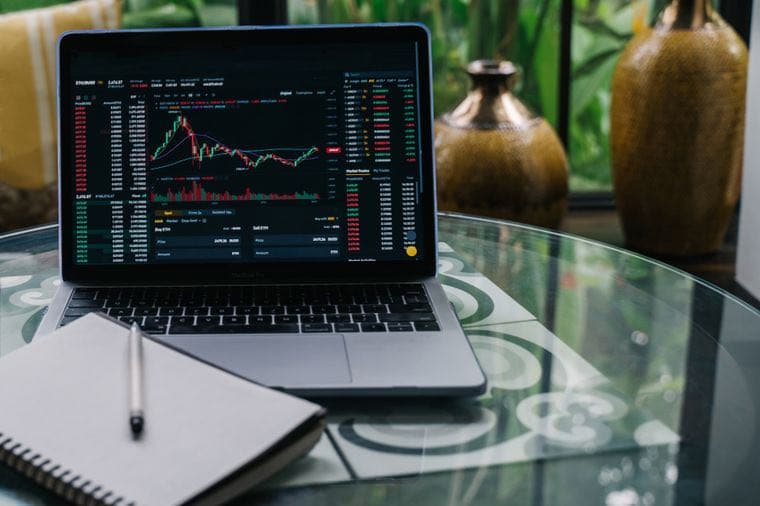 A laptop showing a market chart beside a notebook