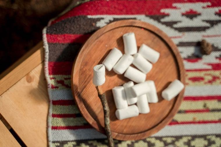 Marshmallows on a wooden plate, one speared on a stick and ready to eat