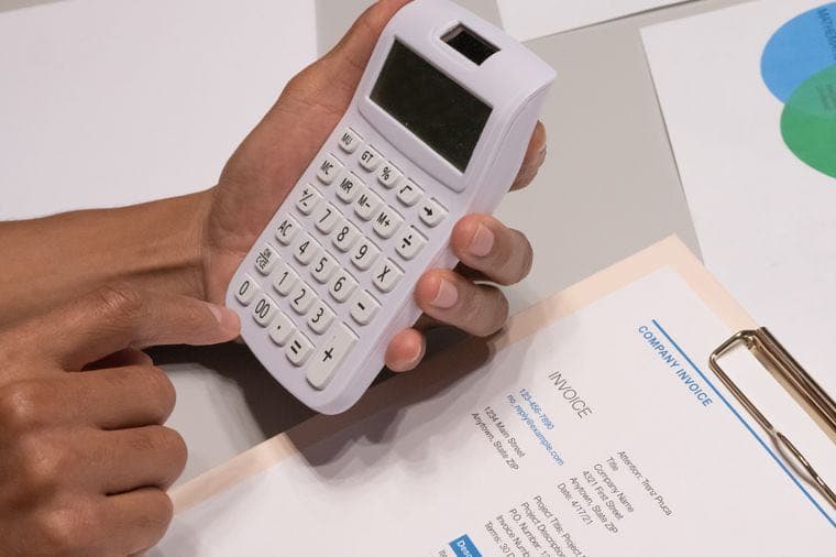 Hands using a calculator over a small business invoice