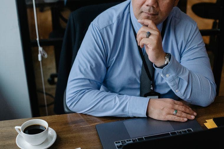 A businessperson thinking at their laptop with a coffee