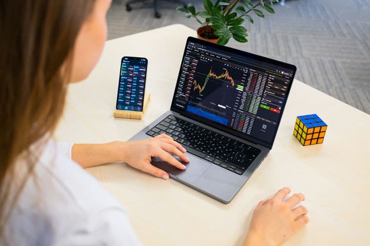 A person checking a share portfolio on a laptop and phone at a desk