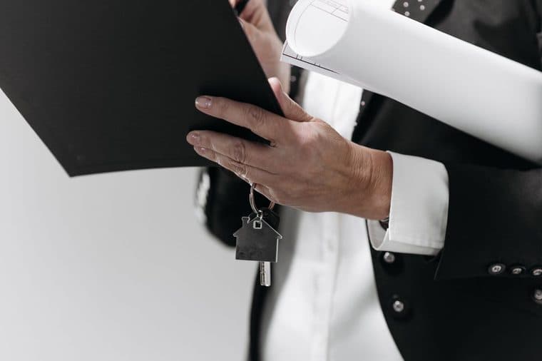 A person in a suit holding property documents and house keys