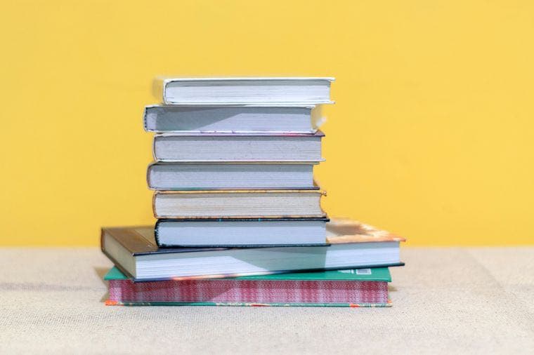 A neat stack of hardcover books against a yellow wall