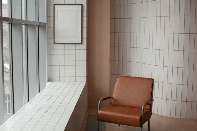 A single leather armchair left by a window in an otherwise empty tiled room