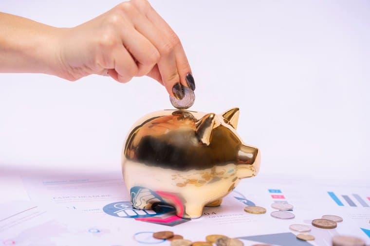 A coin being placed into a piggy bank on top of financial documents