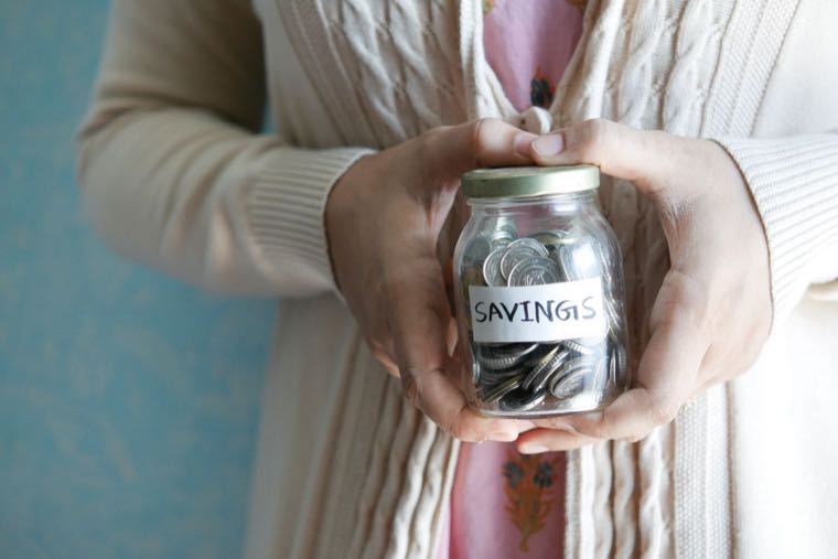 A hand placing money into a jar labelled savings, representing a low-risk place to park cash