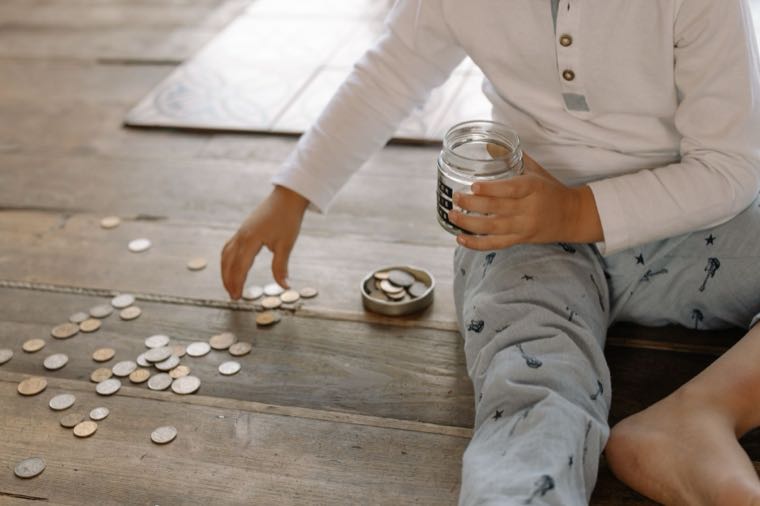 A child putting coins into a jar, learning to save as part of teaching kids about money